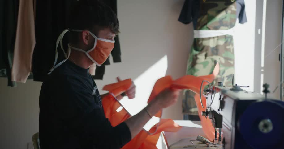A white teenage male sits at a sewing machine table and pulls on a string of flags