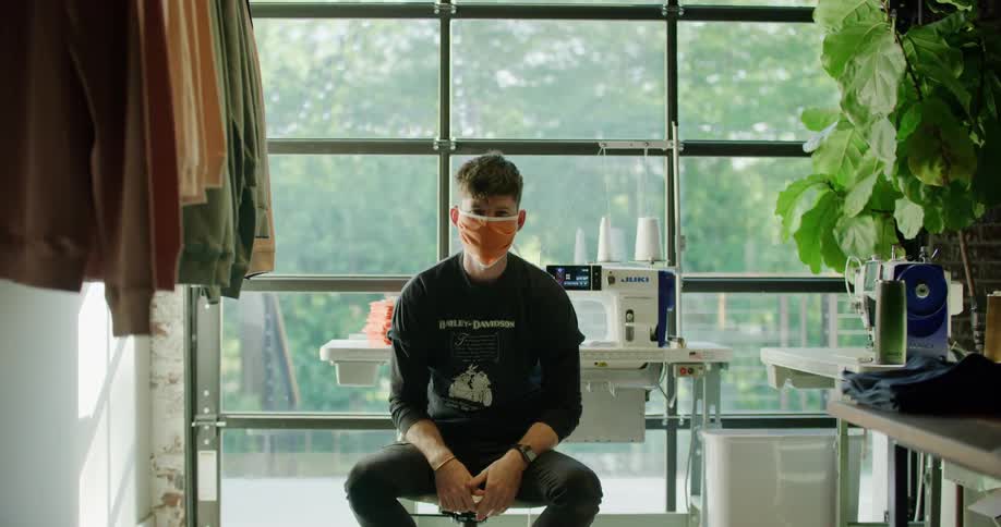 A white teenager sits in front of a sewing machine while wearing a face mask