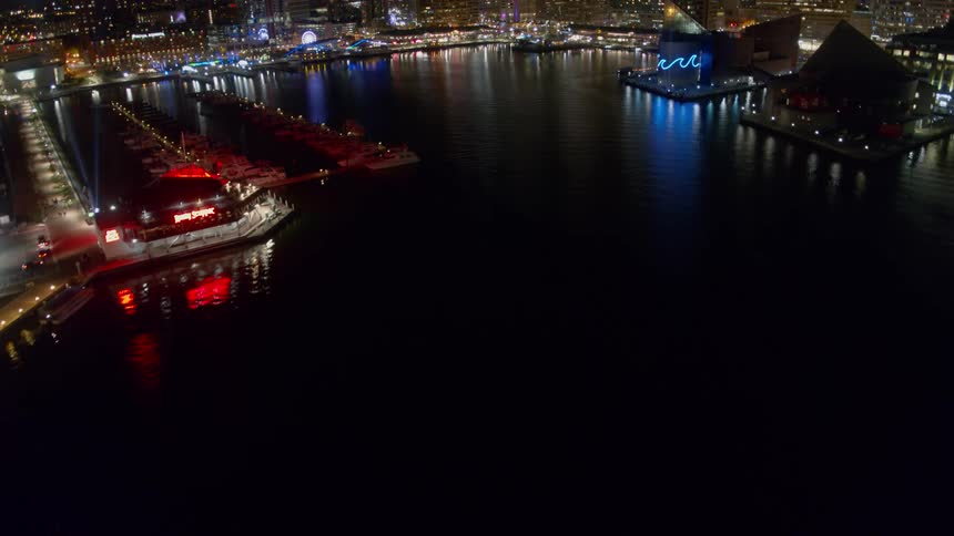 A downtown area of the city that is lit up at night sits next to a harbor