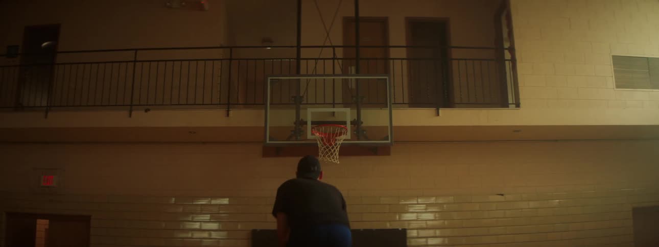 Man wearing baseball cap takes shot in two story gym