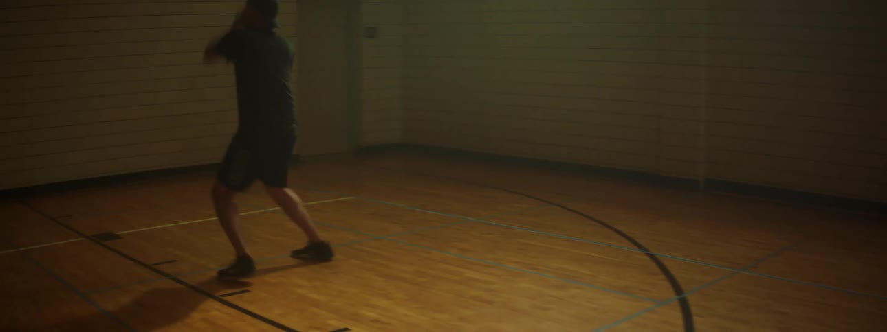 A man dribbling and shooting a basketball by himself on a small indoor basketball court
