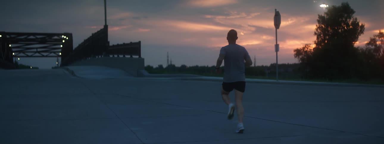 Man running along sidewalk toward bridge at sunset