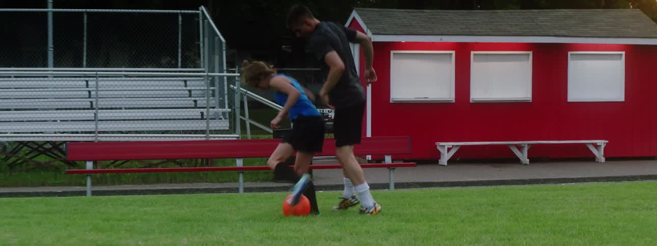 Male and female teenager kicking soccer ball on field