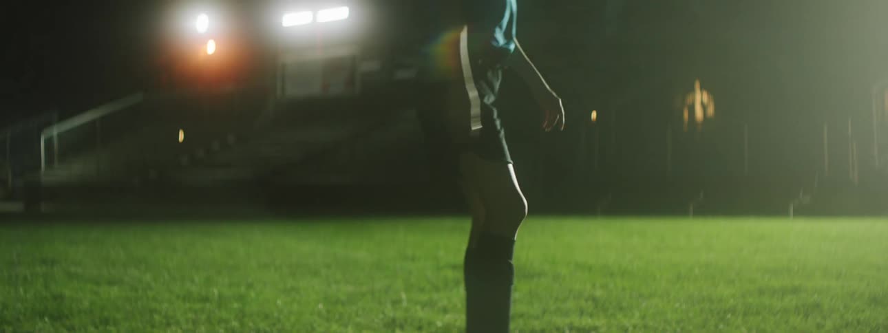 Woman kicks football in stadium at night under the stadium light system