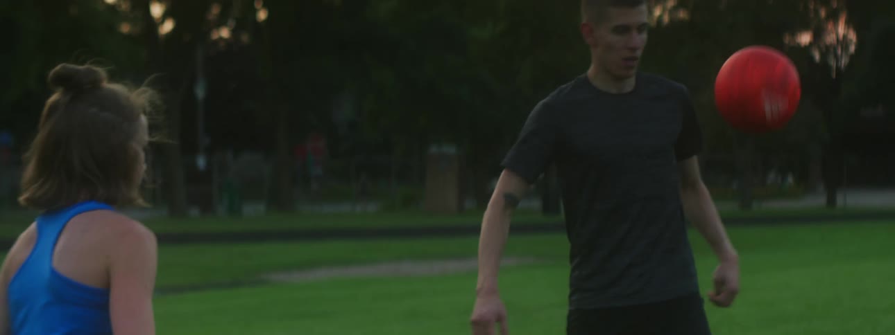 Man and woman play with soccer ball in park
