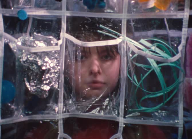 A young girl hides behind a plastic storage sheet