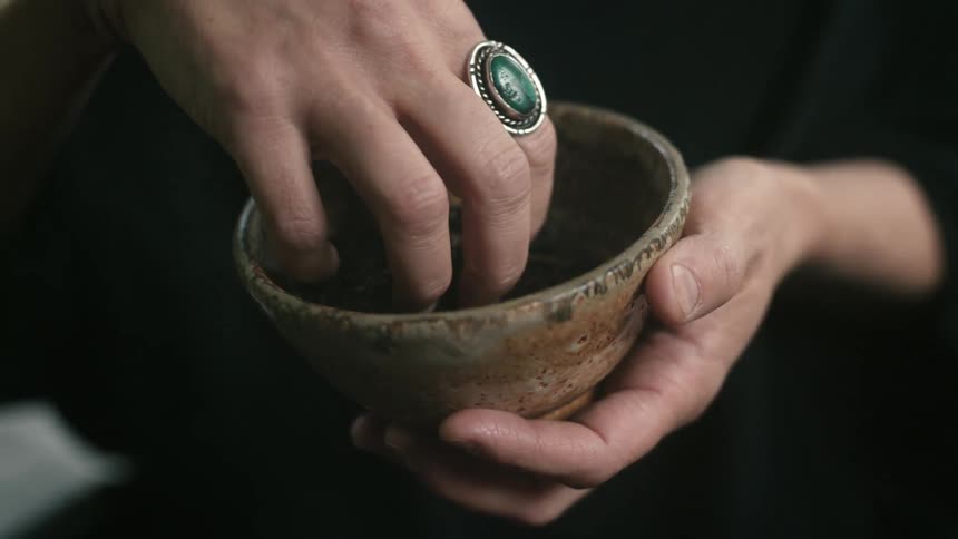 Hand picking up herbs from small brown bowl