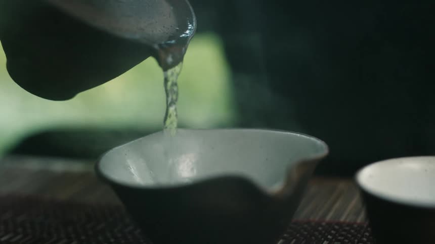 Hot water pouring from small stoneware teapot into cup