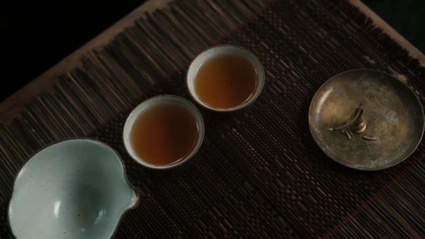 A plate and a kettle sit on a table with an empty bowl and two cups of tea