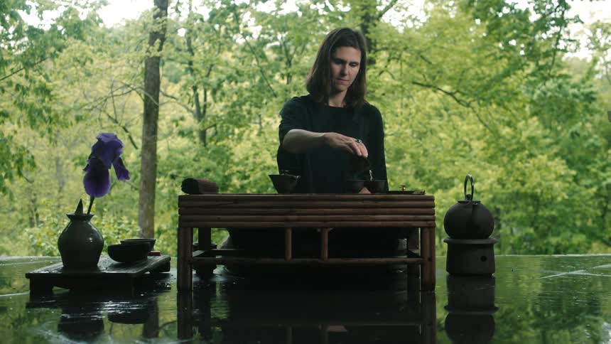 A woman sitting on a mat before a low wooden table performing a tea ceremony