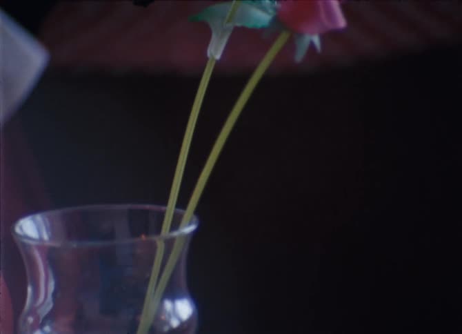 A candle and glass vase with plastic flowers and other gimcracks