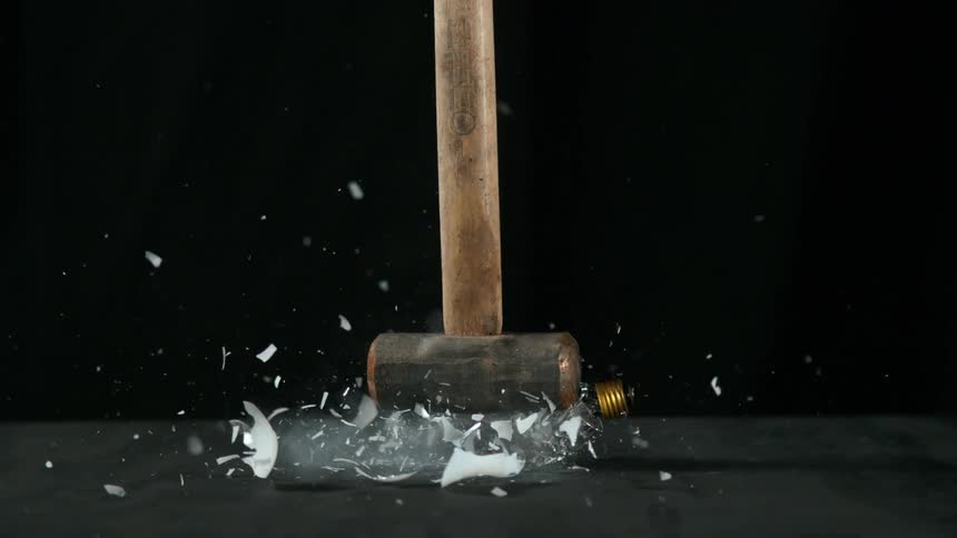 A large hammer falls on and crushes a light bulb