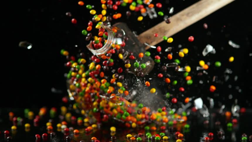 A mallet swings and hits a glass jar filled with candy