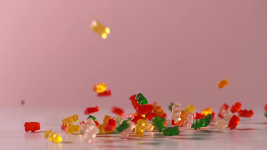 Gummy bears fall in slow motion onto surface in front of pink background
