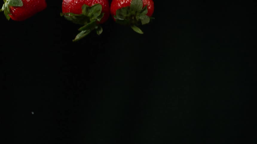 Strawberries falling in slow motion in front of black background