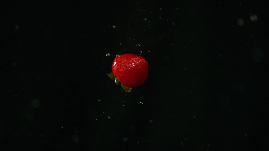 Strawberries with water coming off of them in front of a backdrop in a studio