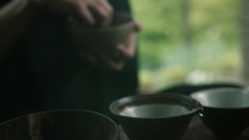 A person takes leaves out of the bowl they are holding and places them in tea cups