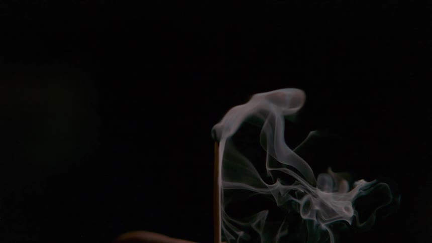 Smoke flows from extinguished match against black background