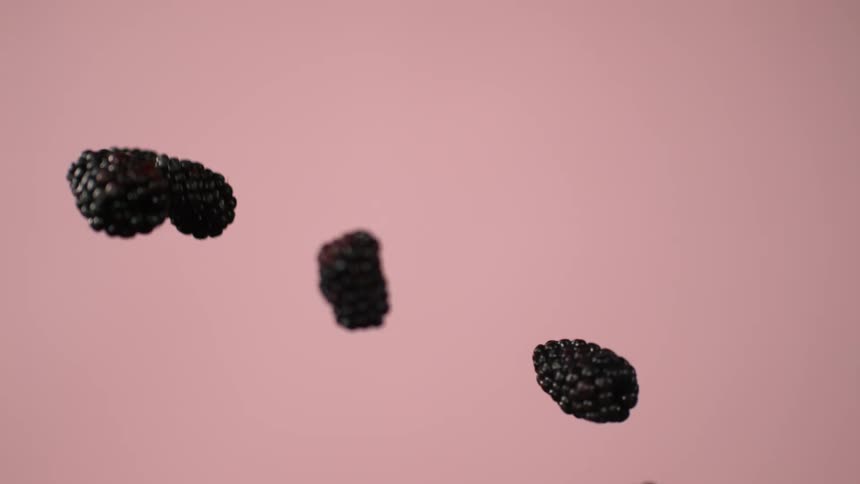 Blackberries fly through the air in front of a pink background