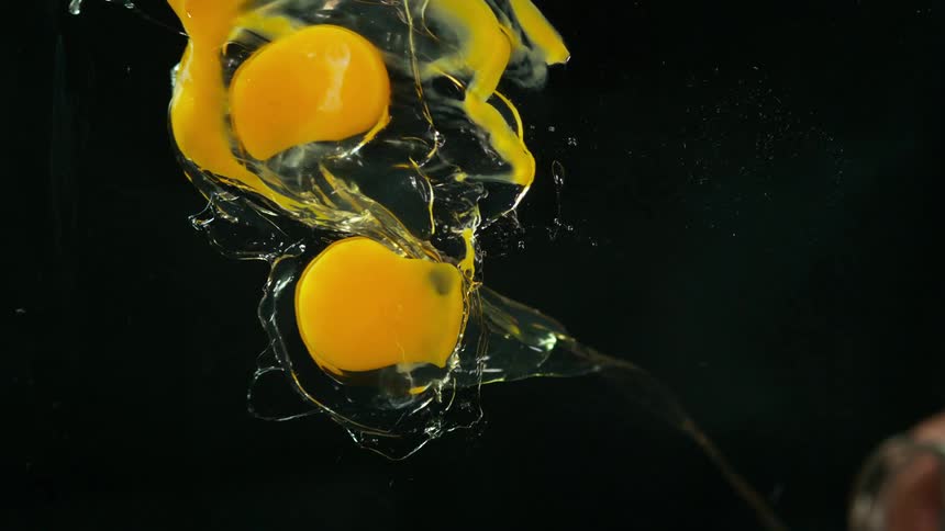 Raw eggs splash into water against black background