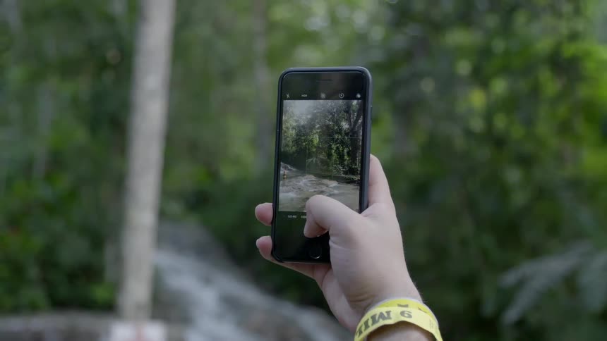 Person recording stream in forest with cell phone
