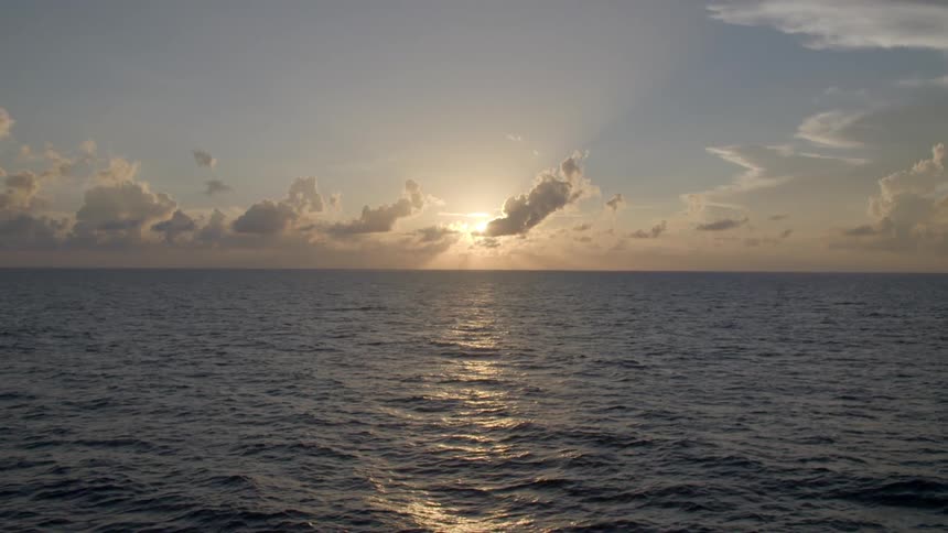 The sun shines over an ocean with clouds in the sky