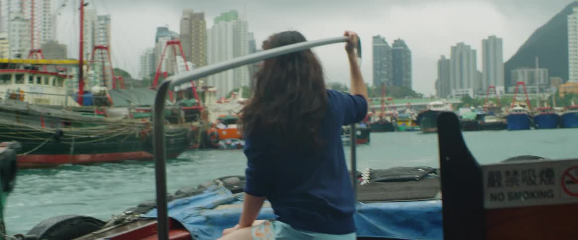 A white woman on a boat takes in a marina packed with other vessels on the coast of a city