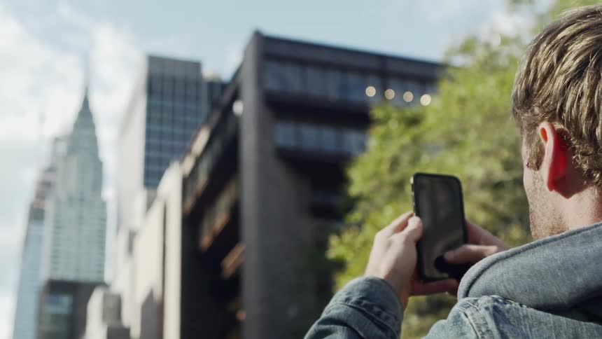 A white male takes a picture of a city skyline with a smartphone