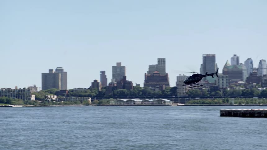 A helicopter flies over a lake with the city skyline in the background