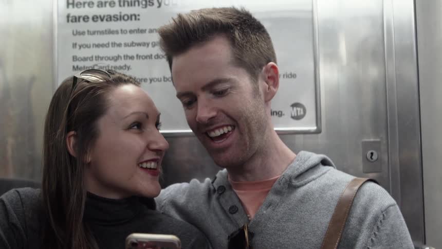 A young man and women are looking at a smart phone and smiling