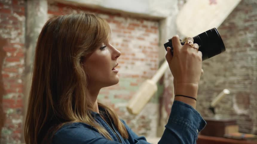Woman aims camera in room with industrial brick walls while talking to someone
