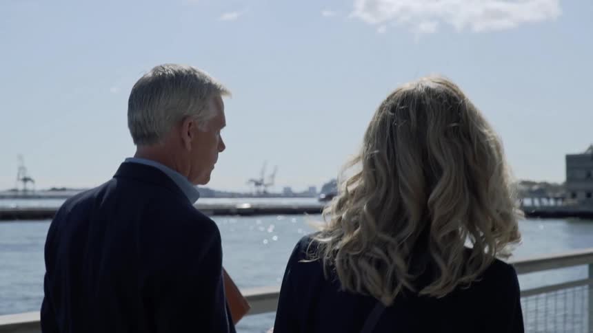 Woman and man in business suit walking on a bridge near a pier