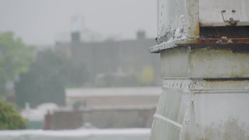 Pouring rain obscures buildings creating drips on metal structure