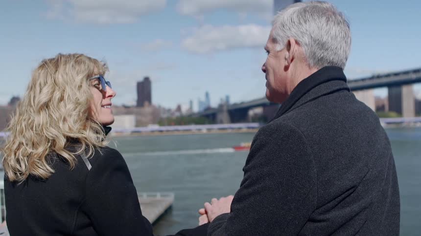 A man and woman stand on a dock and hold hands and smile at one another