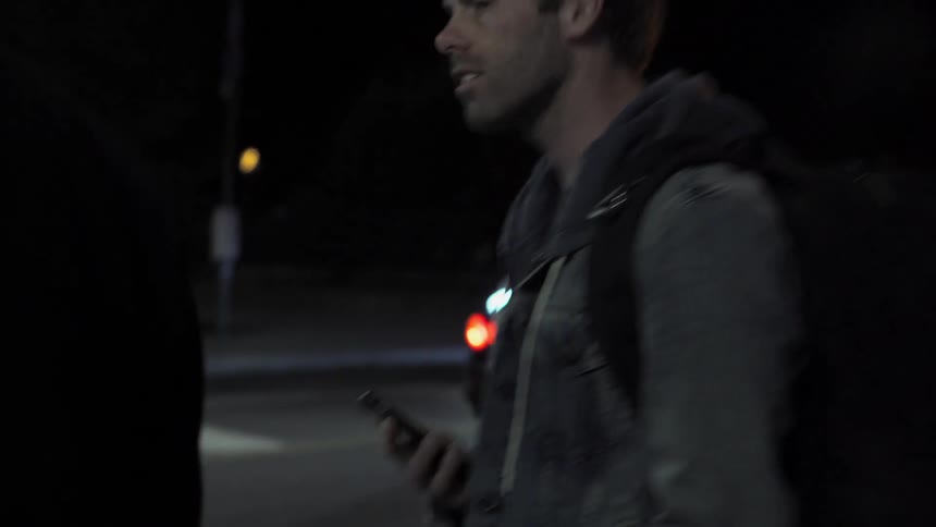 Two white men in a city cross a busy street at night