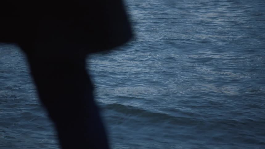 A person walks by an ocean undulating with waves