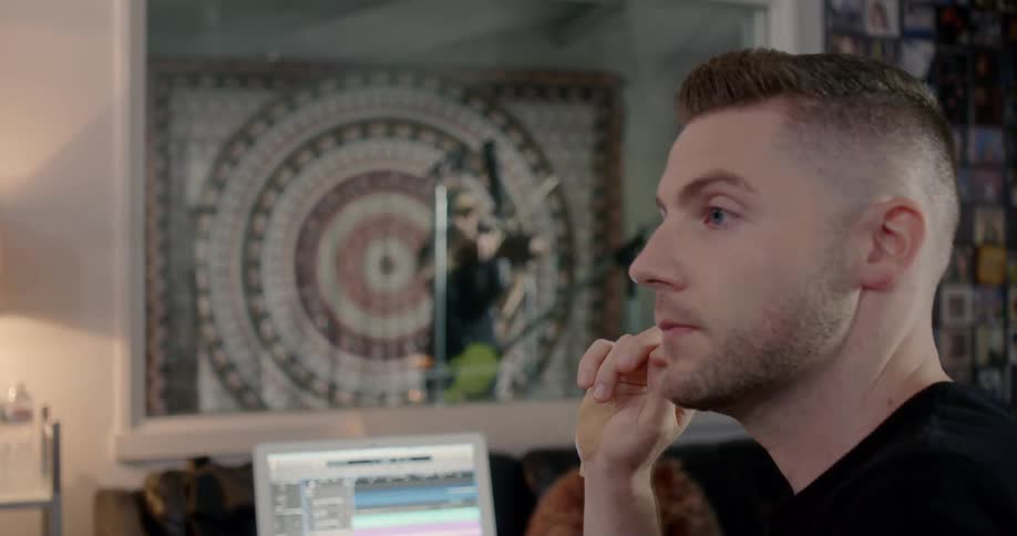 A man listens as a woman plays an instrument in a recording studio