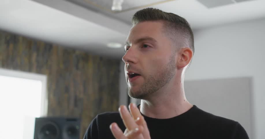 A man stands in a room talking and uses his hands to portray his speech