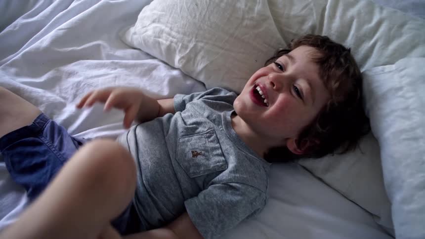 Parent tickles young boy laying on bed