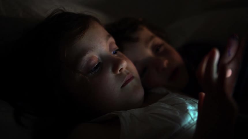 Two young children look at tablet together in the dark