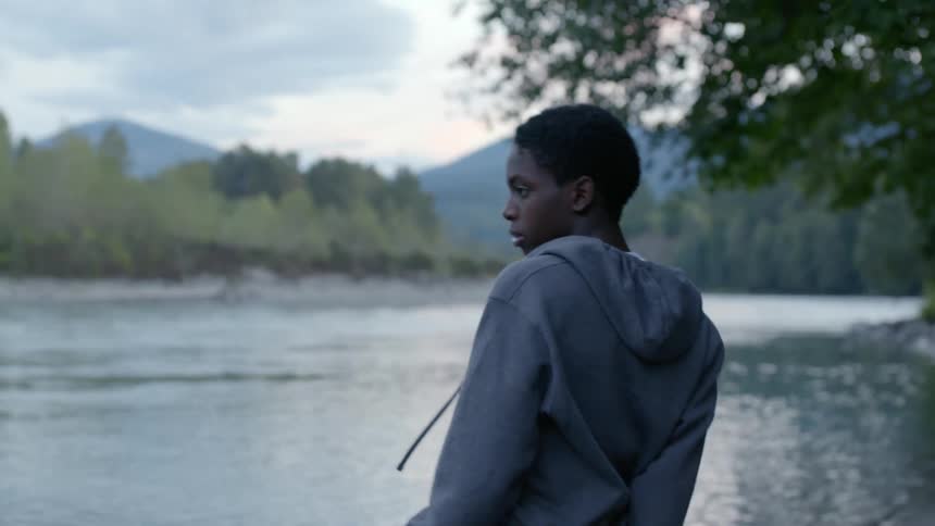 A teenage boy throws a large stick out to the lake in front of hime