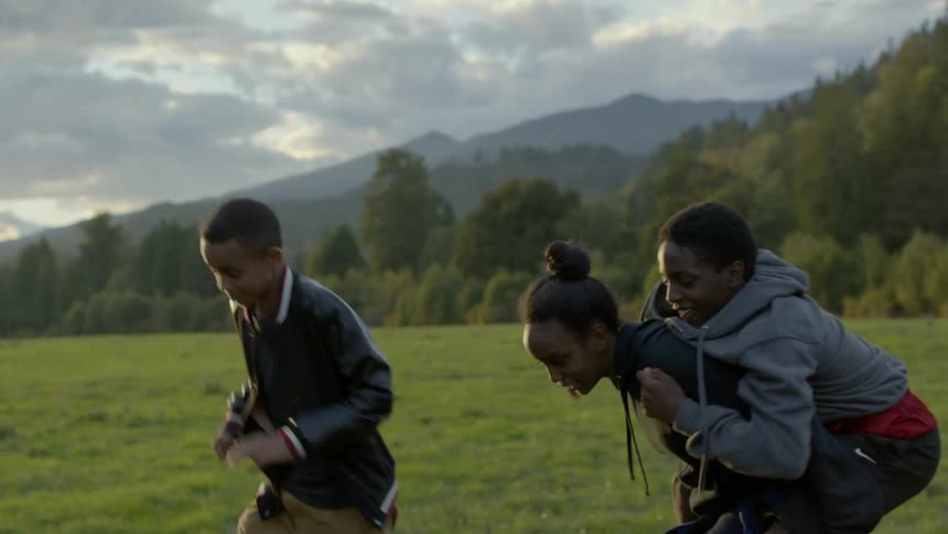 Three teenagers play and rough house together in a rural grass area