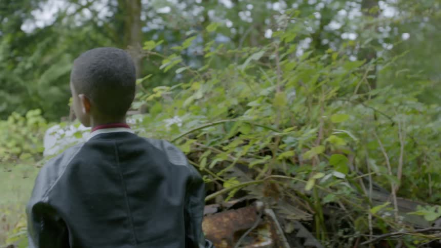 Two boys play around an abandoned car near a forest