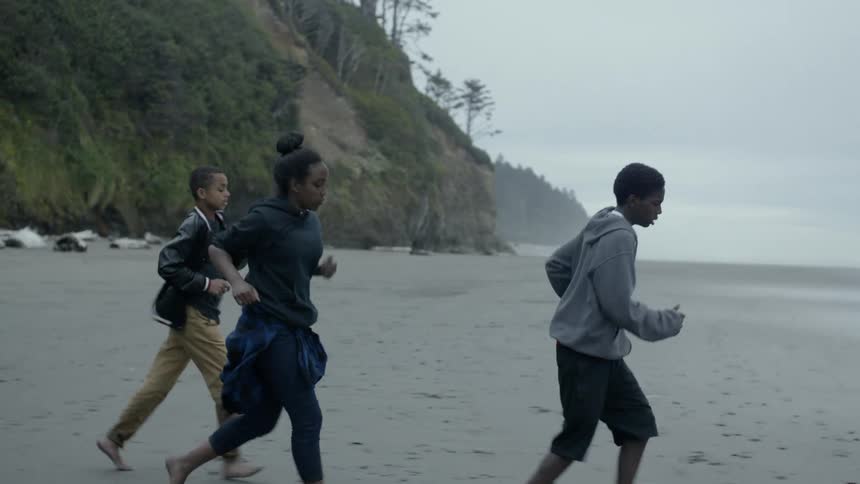 Teenage boys and a girl jog across beach near steep slope on foggy day