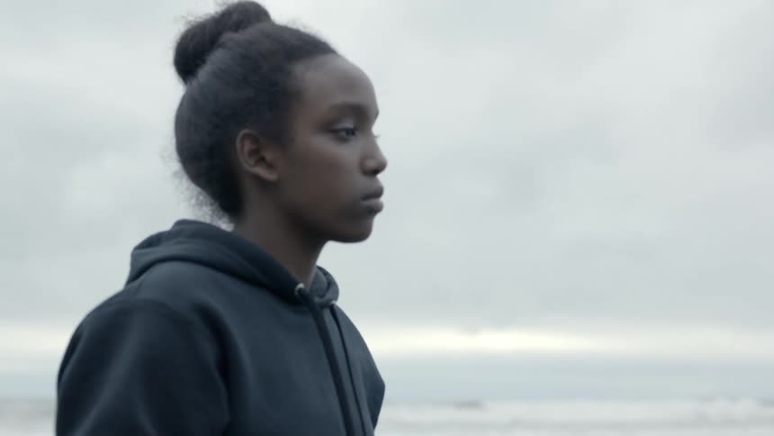 A teenage girl and boy walk along the ocean beach