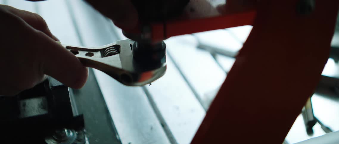 A person uses a wrench to tighten a part onto a base