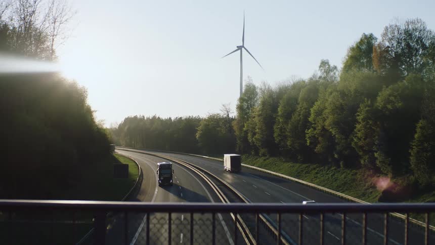 Cars and trucks drive down a highway past a wind turbine