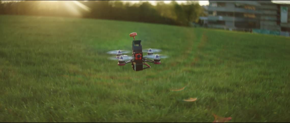 Small drone hovers and lifts upward over field at dawn
