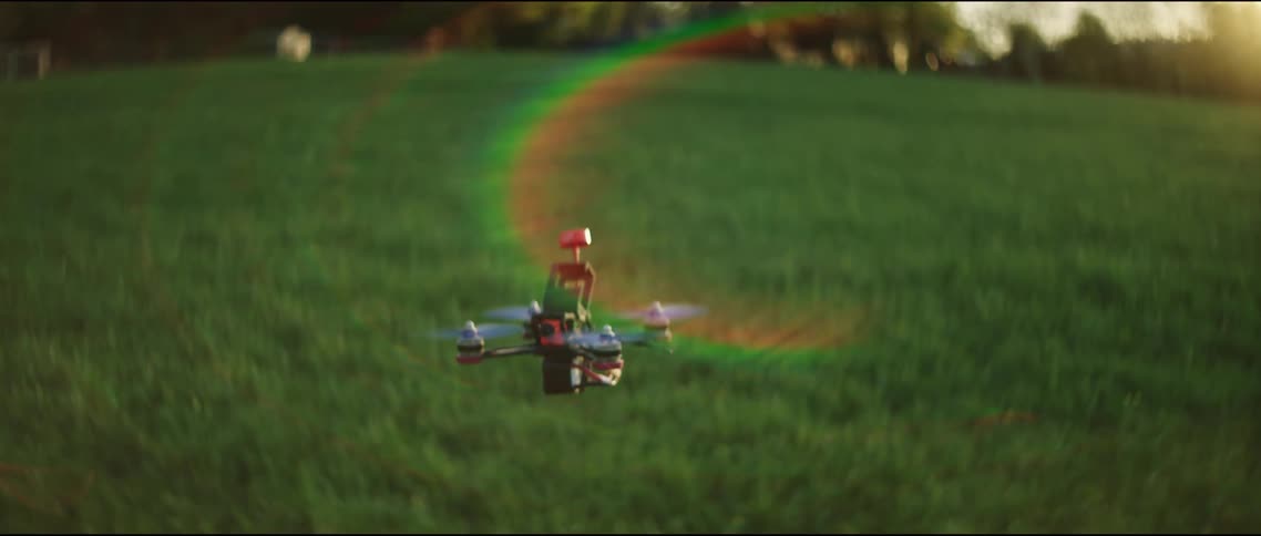 A drone hovers and flies over the green grass of a field on a sunny day