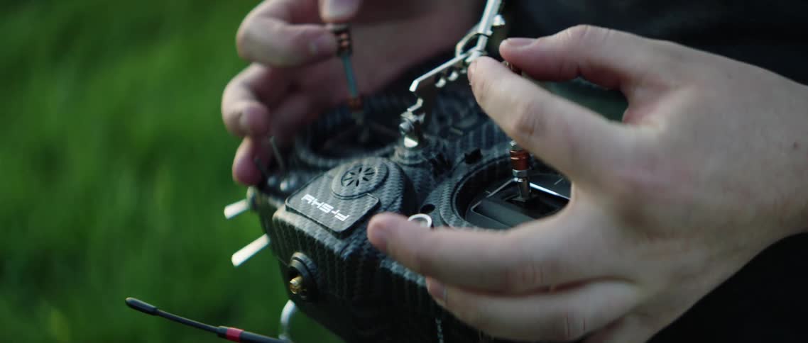 Person stands outdoors on grass manipulating remote controller
